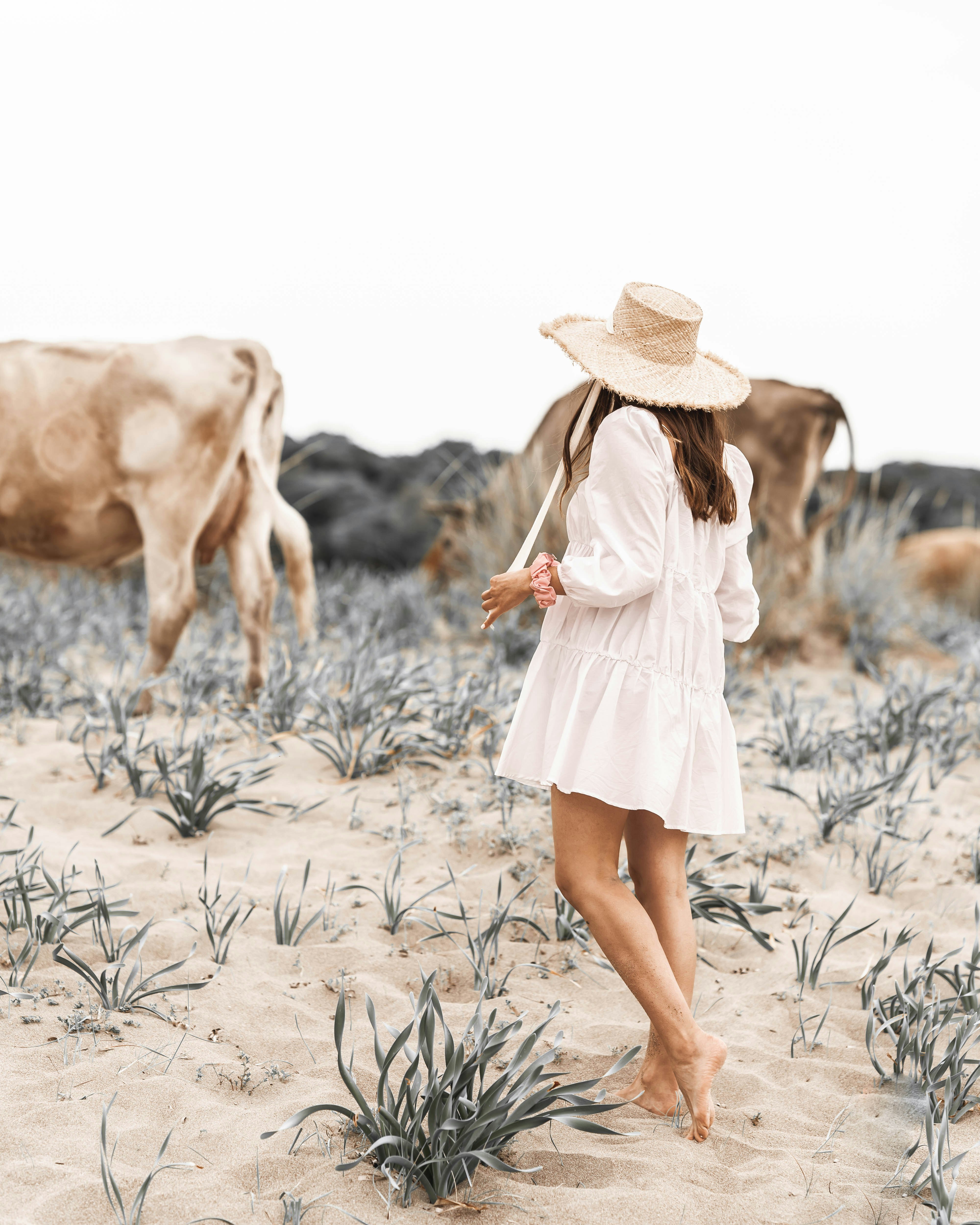 woman in white dress and brown hat walking on brown sand during daytime